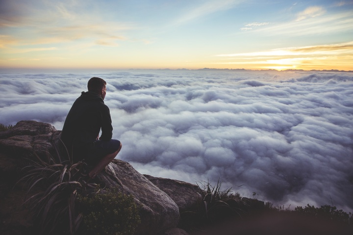 A man sitting on a rock looking out over the clouds covering a valley.