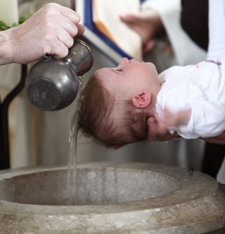 A young baby being baptized with water pouring over the child's head.