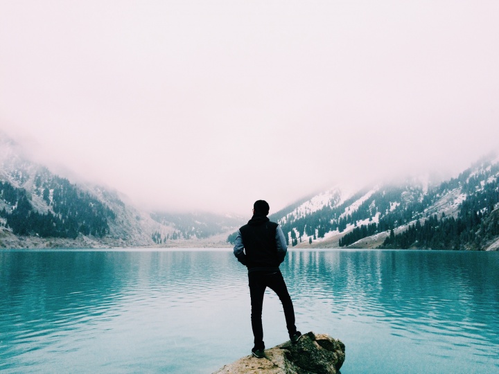 A man staring a clear blue lake.