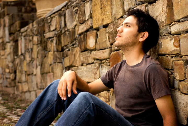 A young man sitting against a rock wall.