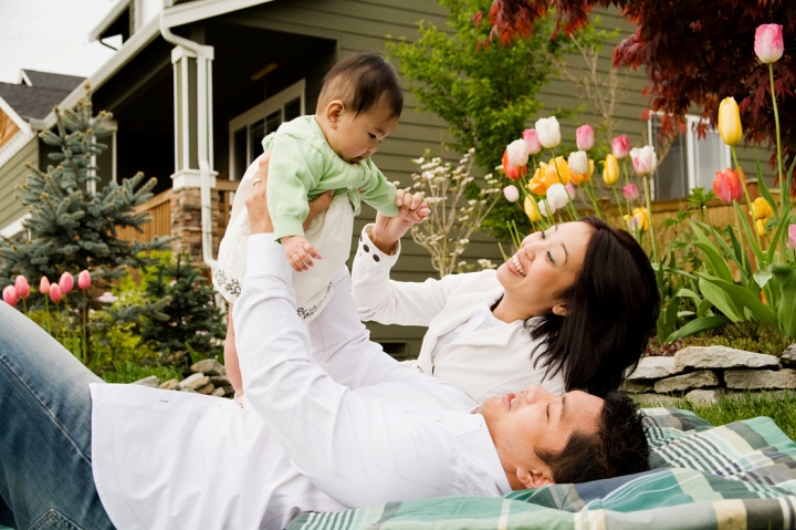 A family with a baby laying on blanket outside playing.