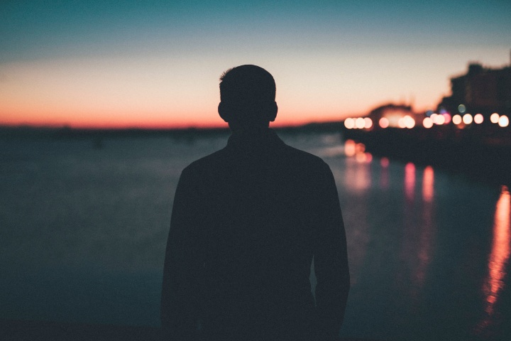 A silhouette of young man looking out over a body of water.