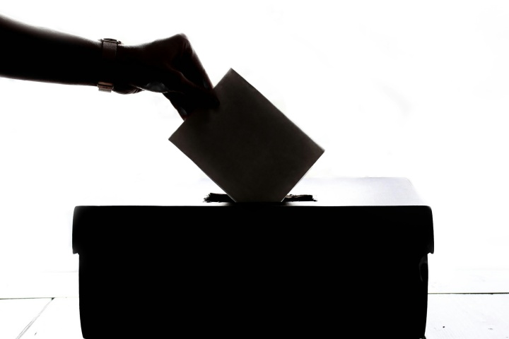 A photo illustration of hand inserting a vote card into a box.