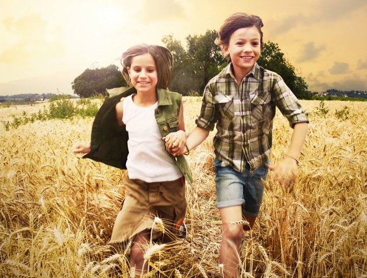 Two kids running through a tall grass field.