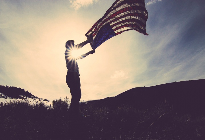 A man holding an American flag flapping in the wind.