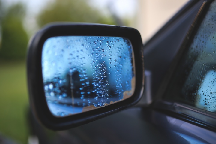 A car's side mirror cover with rain drops.