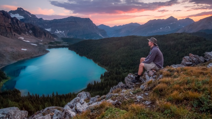 A young man sitting on rock looking out over mountain vista.