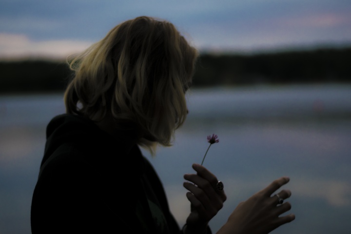 A woman holding a wilting flower in her hand.