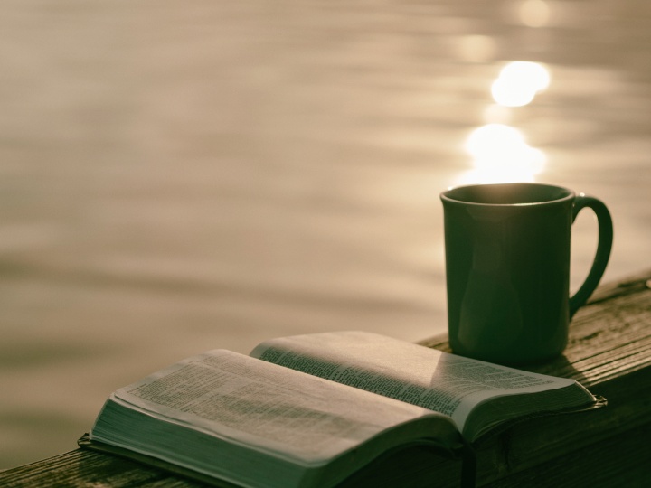 An opened Bible beside a coffee mug.