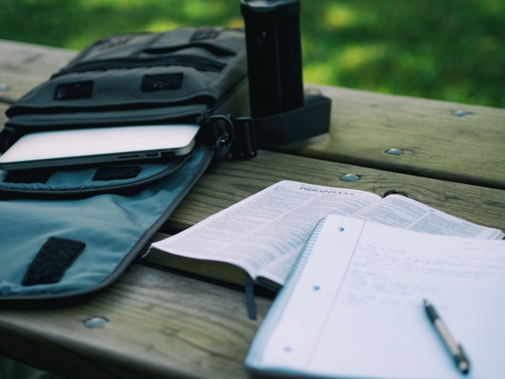 A Bible and notebook laying on a table. A laptop is in backpack.