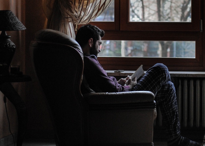 A man sitting in a big chair by a window reading.