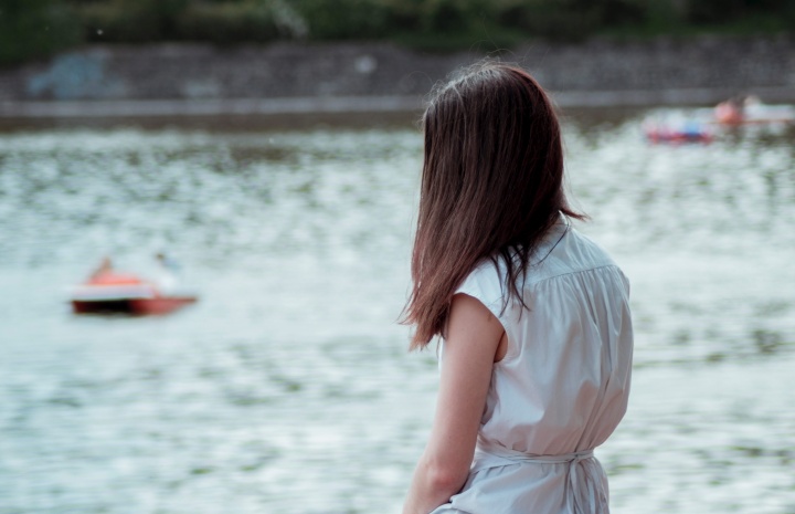 A teen girl sitting by a small pond looking out over the water.