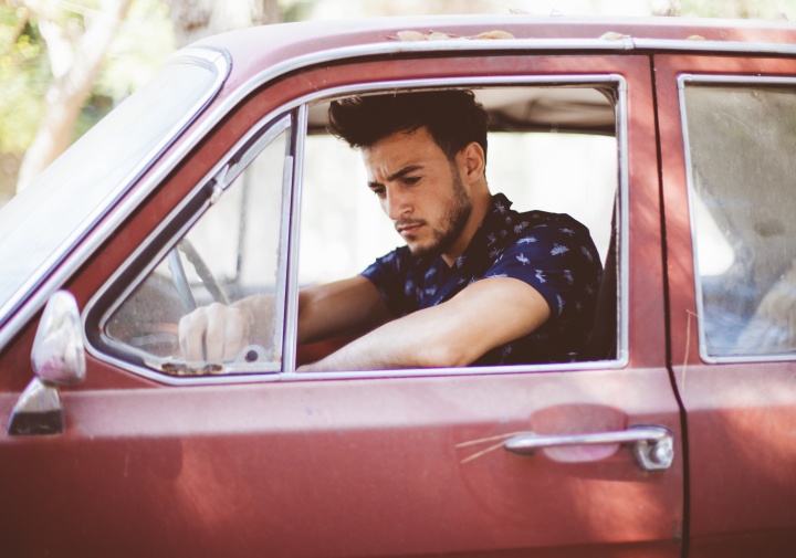 A young man sitting in the driver's seat of an old car.