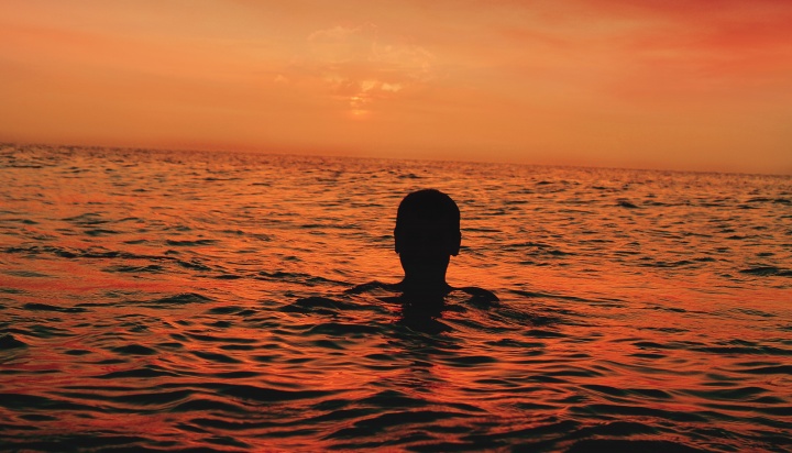 A person floating in the water with the sun setting.
