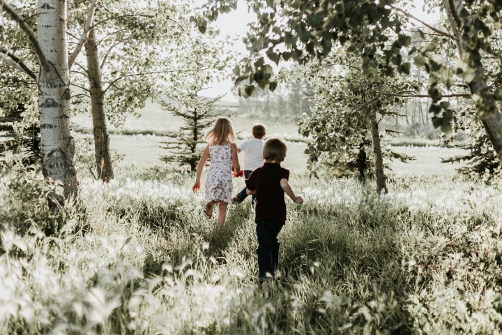 Three kids running through a field. 
