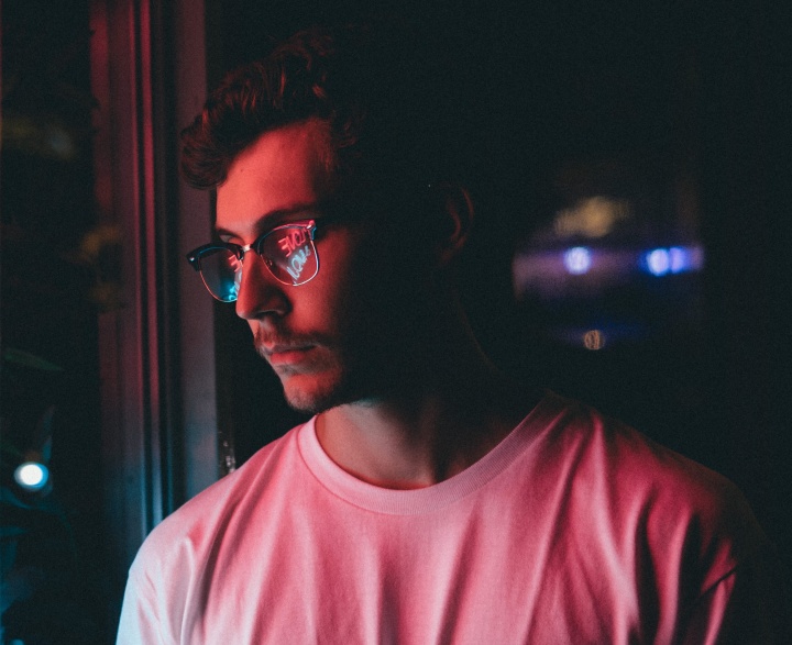 A young man staring at neon sign on a window.