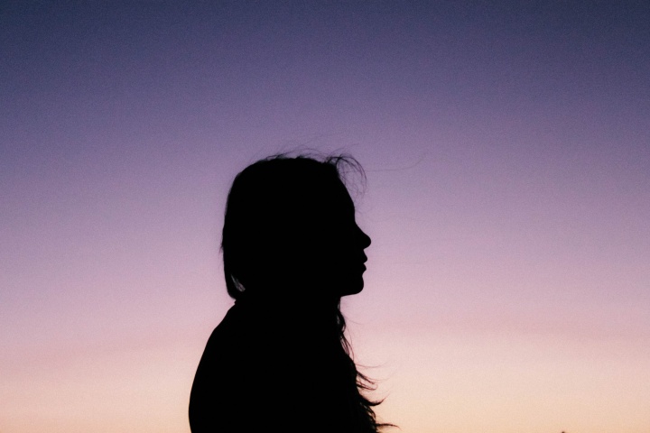 A silhouette of young woman with the sun setting in the background.