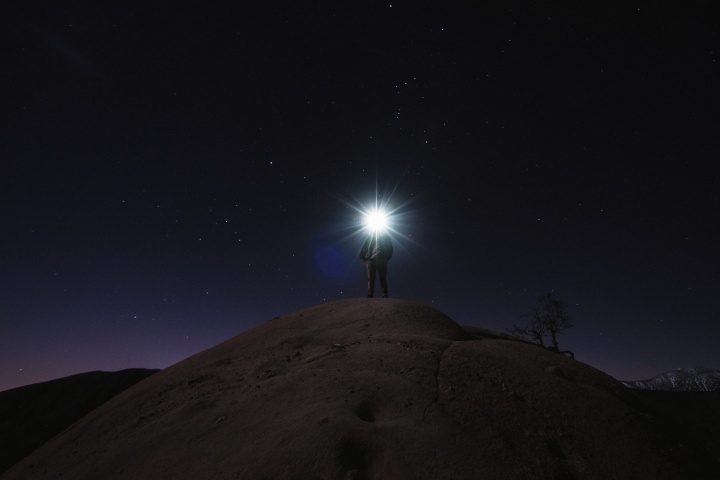 A person with a head lamp shining bright in the darkness.