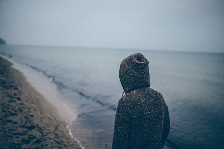 A person walking on a beach wearing a hoodie.