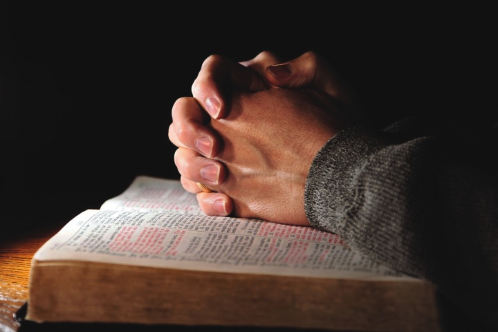 Clasped hands on top of an open Bible.