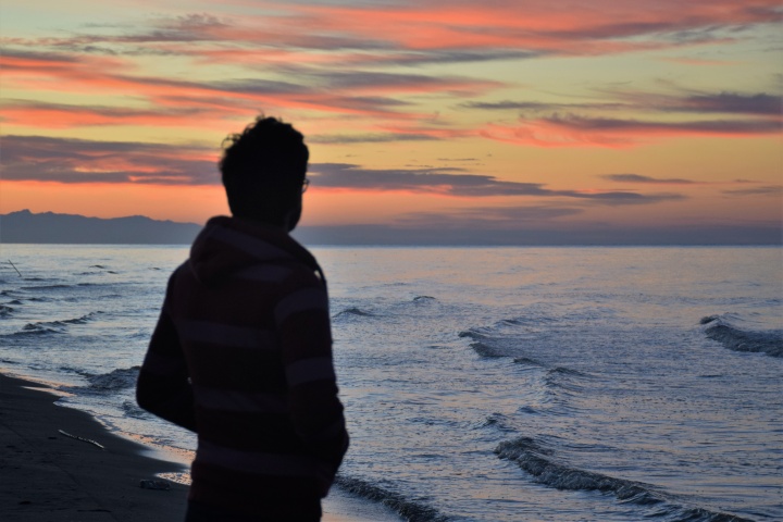 A man looking at a sunset over a body of water.