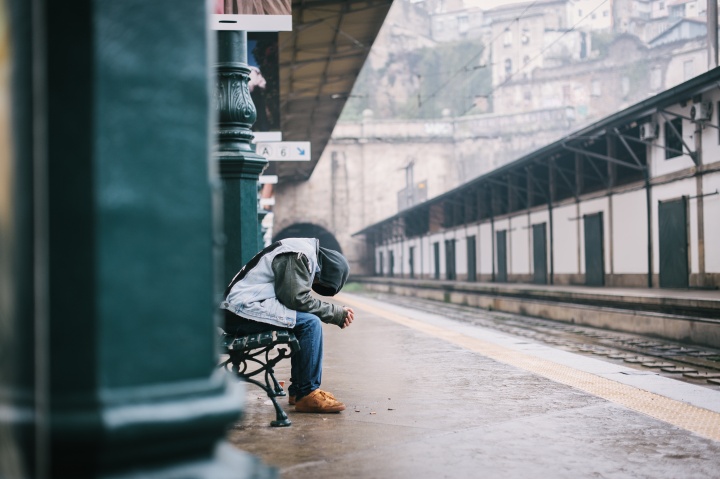 A man sitting a train terminal with his head down.