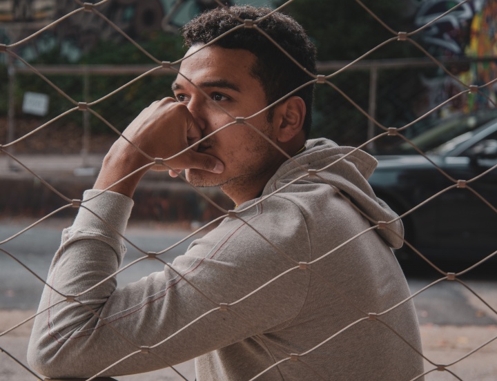 A young man sitting next to chain fence with his head on his hand.