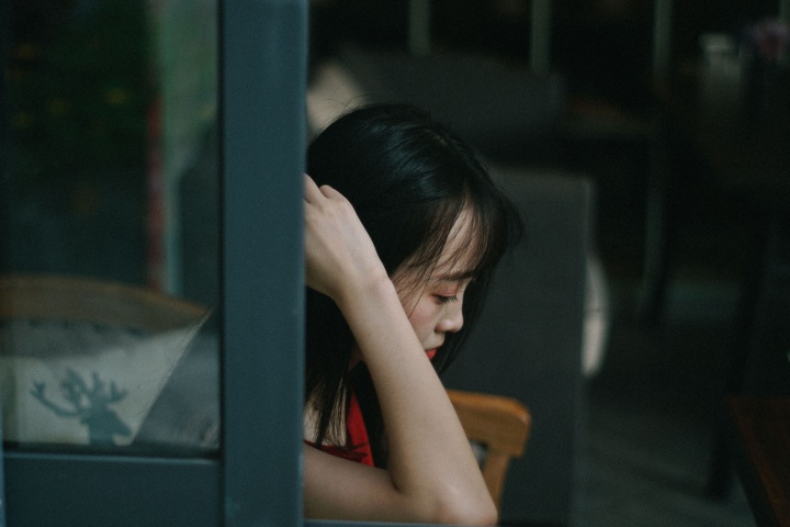 A woman looking depressed sitting by a window.