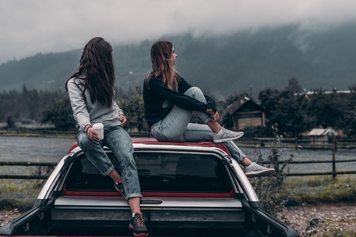 Two young adult women sitting on top of a car.