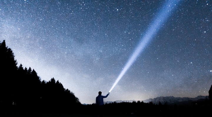 A person pointing a flashlight beam up into the night sky.
