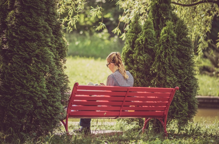 A woman reading while sitting on a red bench.