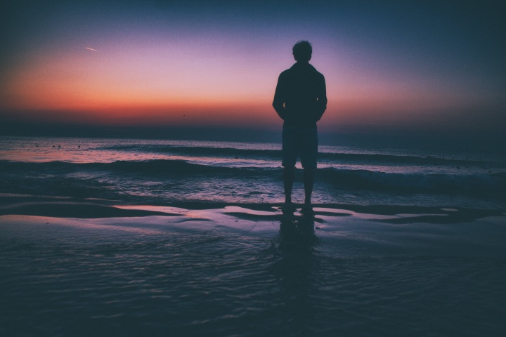 A man standing by a lake at sunset.