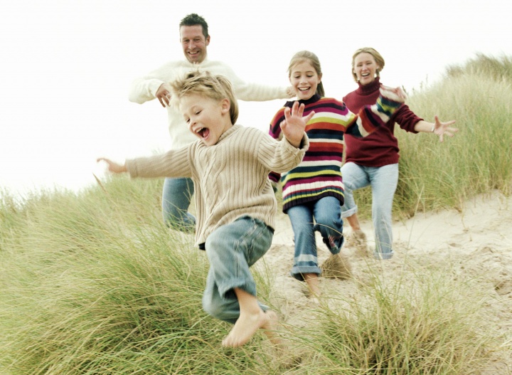 A family running on sandy beach with grass.