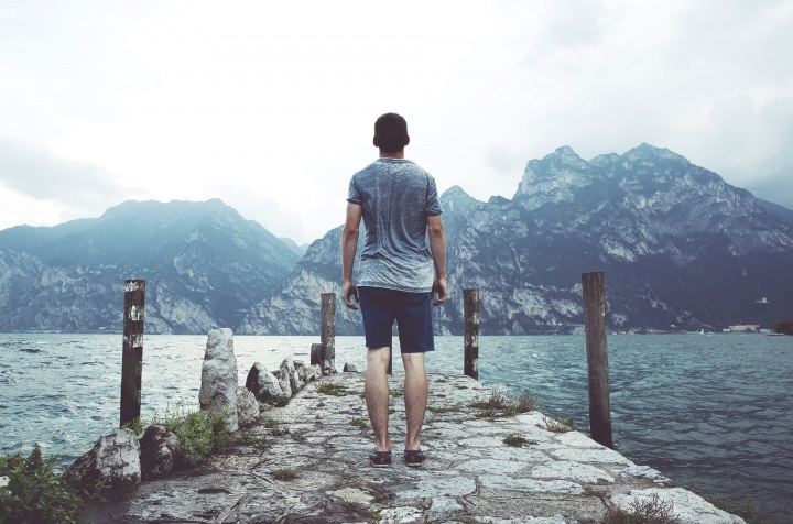 Photo of man standing on a stone dock on a lake surrounded by mountains.