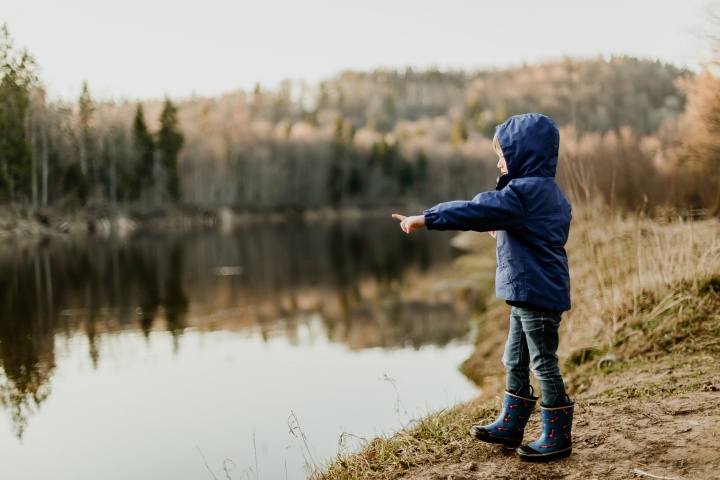 A little child standing by a lake pointing.