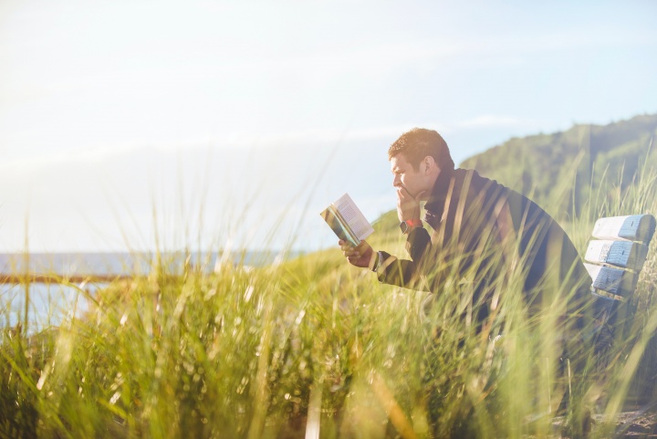Man sitting in field studying Bible alone.