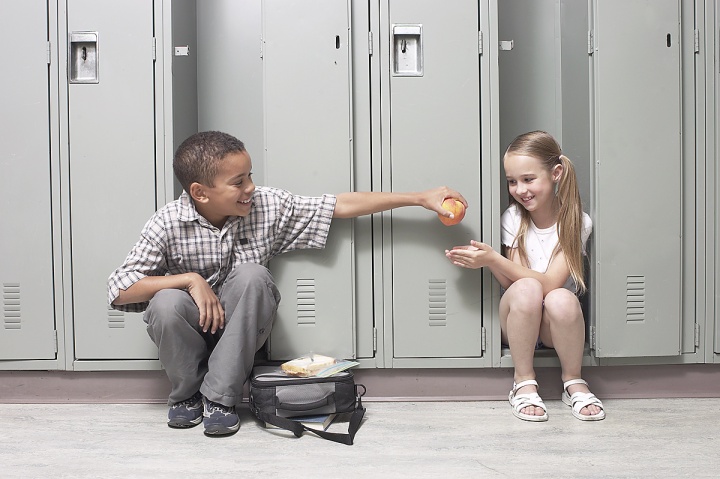 A young boy giving an apple to girl a school.