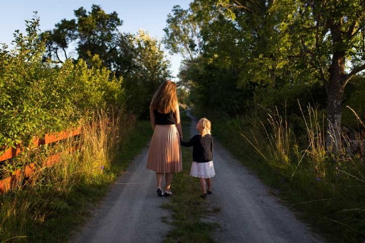 A woman and a child walking outdoors on a path through the trees