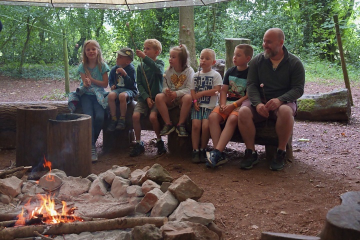 A group sitting by a campfire beneath a shelter