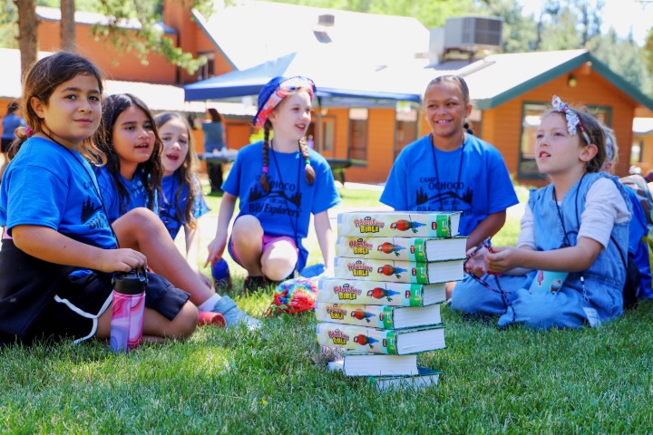 a group of girls sitting around a stack of Bibles