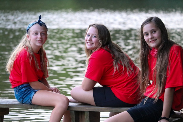 three girls sitting on a bench by the lake