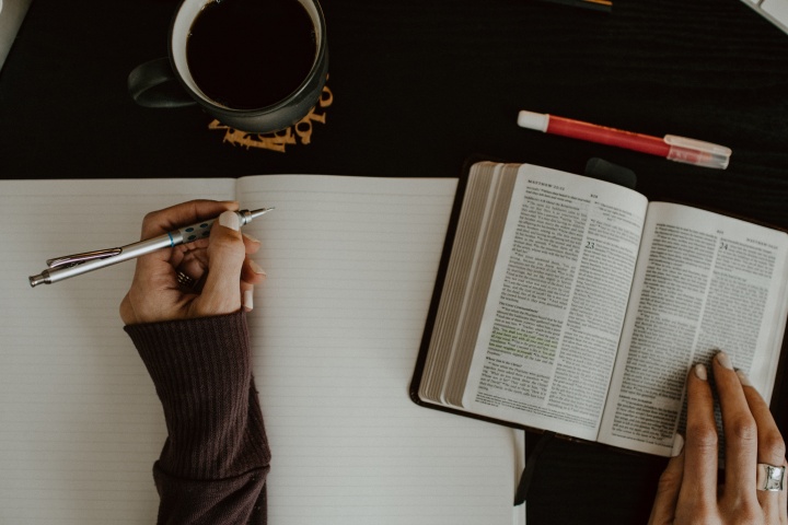 A pair of hands with a pen and an open Bible and blank notebook