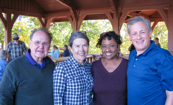 four people smiling and standing under a picnic shelter