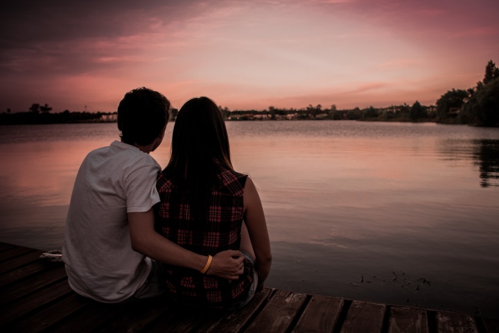 Girl and guy sitting on a dock looking at the sunset