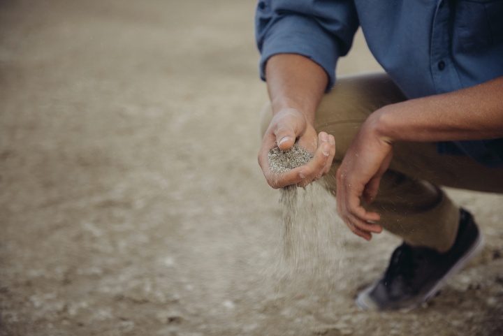 a man crouching close to the ground and sifting grains through his hand.