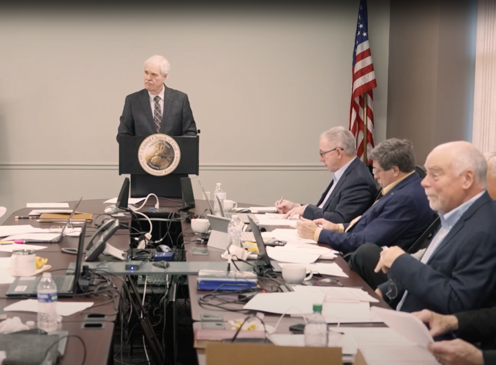 a group of elders seated at a table while listening to a speaker at a podium