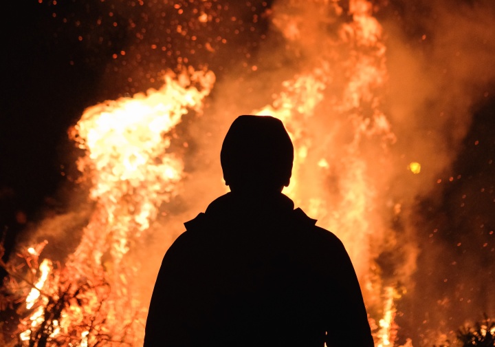 the silhouette of a person standing in front of leaping flames of fire