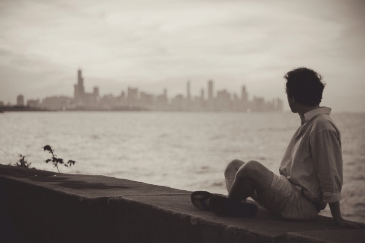 a man sitting cross-legged in a concrete ledge overlooking a body of water an a distant city skyline