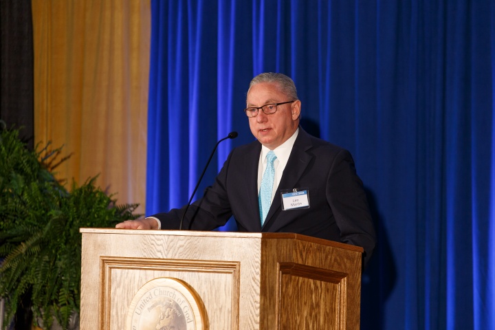 Len Martin standing at a podium with a blue curtained backdrop