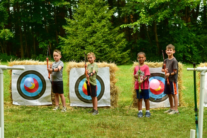 four boys holding bows as they stand in front of archery targets